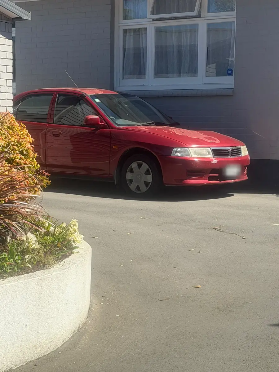 Red 2000 Mitsubishi Lancer sedan parked in an Ilam driveway