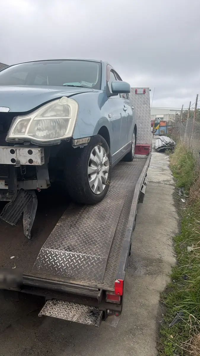 The same Nissan Bluebird Sylphy loaded on a trailer, front bumper missing